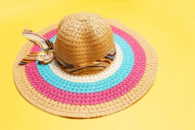 Close-up of women summer hat with ribbon bow and lines of white, pink and blue colors on yellow background.