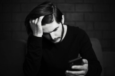 Akıllı telefondan bakan üzgün adamın yakın çekimi. Siyah beyaz portre.