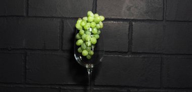 Şarap kadehindeki yeşil üzümlerin resmi, siyah tuğla duvarda izole edilmiş..
