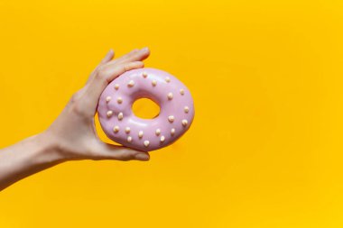 Turuncu arka planda pembe bir donut tutan bir kadının yakın çekimi..