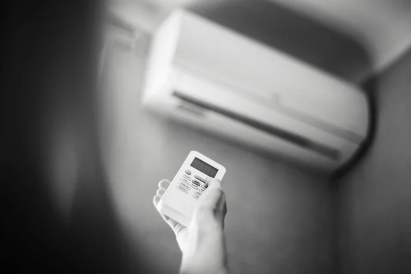 Black and white photo of hand adjusting air conditioner with remote control.