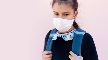 Yüzünde, pembe arka planda tıbbi maske takan okul kızının portresi..