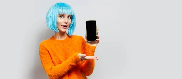 在灰墙上挂着一个拿着智能手机的年轻蓝头发女孩的工作室肖像 — 图库照片