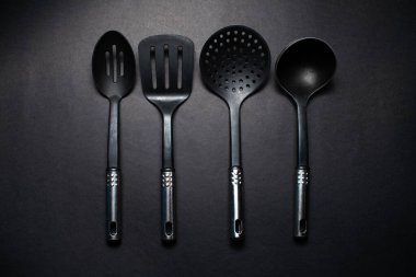 Masanın üzerinde krom saplı siyah mutfak aletlerinin stüdyo resmi var..