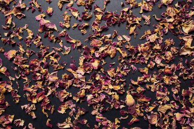 Stüdyo fotoğrafında siyah masanın üzerinde kurumuş çay gülü yaprakları var..