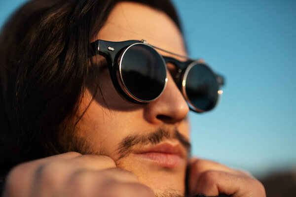 Close-up portrait of young guy with black sunglasses, on the back of blue sky.