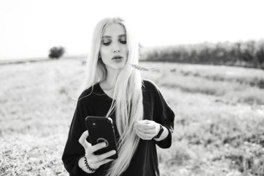 Sahada elinde akıllı telefon tutan sarışın bir kızın siyah beyaz fotoğrafı..