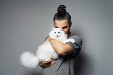 Gri arka planda beyaz kedisi olan genç bir adamın stüdyo portresi. Mavi gözlü evcil hayvan.