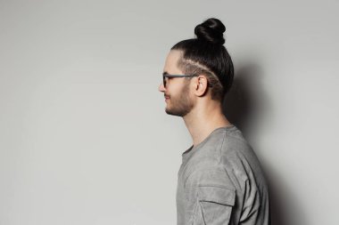 Stüdyo profil portresi. Gri arka planda saç topuzu olan genç bir adam..