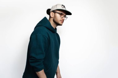 Stüdyo profil portresi gözlüklü, şapkalı ve kapüşonlu süveter giyen genç adam..