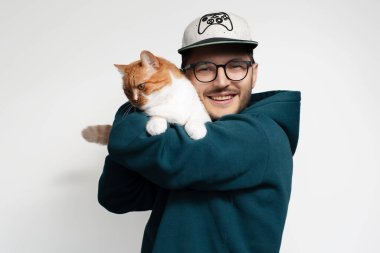 Kırmızı beyaz kedisine sarılan mutlu genç adam, beyaz arka planda izole edilmiş.