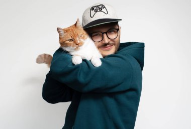 Kırmızı beyaz kedisine sarılan mutlu genç adam, beyaz arka planda izole edilmiş.