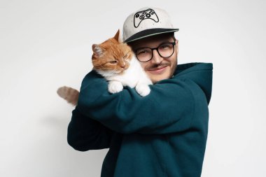 Kırmızı beyaz kedisine sarılan mutlu genç adam, beyaz arka planda izole edilmiş.