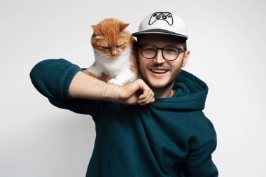 Kırmızı beyaz kedisiyle oynayan mutlu genç adam. Beyaz arkaplanda izole.