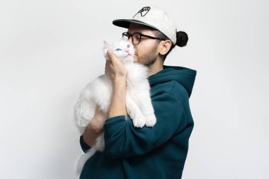 Mutlu genç adam beyaz arka planda beyaz kedisini öpüyor..