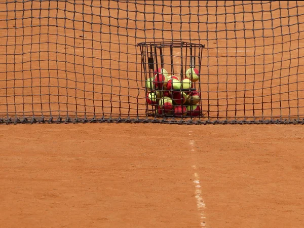 Basket with balls and net on the clay tennis court