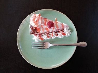 Kremalı ve kirazlı kek ve yeşil tabakta çatal.