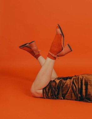 Stüdyodaki kızıl saçlı kıvırcık kız turuncu arka planda şık kıyafetler giyiyor.