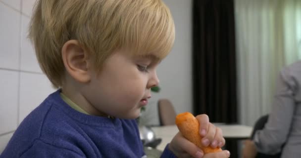 Niedliches Kleines Kind Isst Große Möhre Küchentisch Während Mutter Hause — Stockvideo