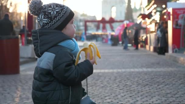 Éhes Magányos Gyerek Banánt Eszik Karácsonyi Piacon Egyedül Állva Téli — Stock videók