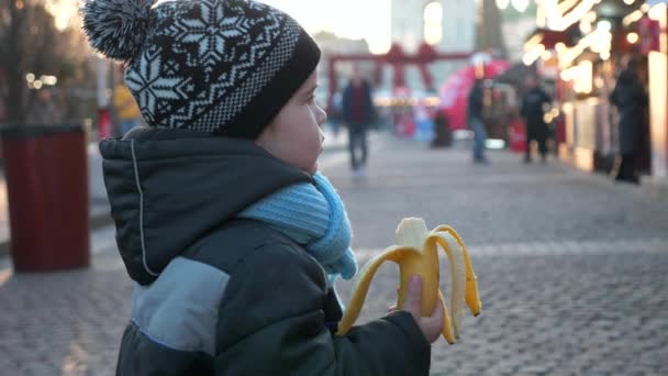 Éhes Magányos Gyerek Banánt Eszik Karácsonyi Piacon Egyedül Állva Téli — Stock videók