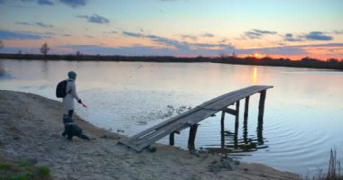 Anne ve Çocuk, Nehir Gölü kıyısındaki Tahta Balıkçı İskelesi yakınlarında Kum Atın. Manzaralı Günbatımı Bulutu Yansıması Güzel Akşam Manzarası