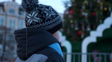 Küçük çocuk Noel ağacına bakıyor. Kış Tatil Akşamı Şehir Meydanı. 2x Yavaş çekim 60 fps 4K