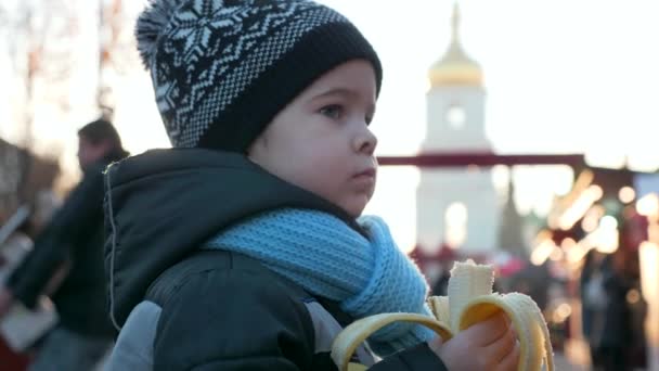 Hungry Lonely Child Eats Banana Christmas Market Standing Alone Winter — Stock Video