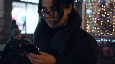 Uyanış Sokağı 'nda Uyanış sırasında Sosyal Medya' yı İzleyen Ciddi Kadın. Kış Tatili Akşam Şehri. 2x Yavaş çekim 60 fps 4K