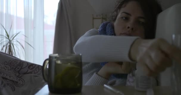 病気の女性はベッドルームの窓の前にベッドの上に横たわっている間 水の薬ガラスを取ります4K — ストック動画