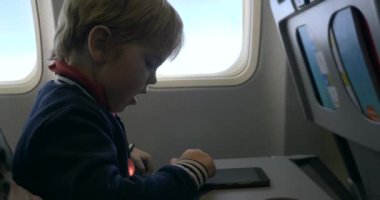 Küçük çocuk akıllı telefon dokunmatik ekranı kullanıyor. Çocuk, uçuş sırasında yolcu koltuğunda oturur.