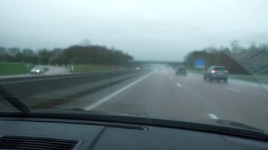 4K 60p yakın plan ön cam silecekleri yağmur damlalarıyla ıslak ön ekran boyunca süpürülüyor. Yağmur yağarken araba kullanmak. Otoyolda ilerliyoruz. Köy yolu. Fransa Avrupa