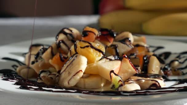 Close-up Pouring Chocolate Cacao Cream on Raw Fruit Salad Dessert of Bananas Orange Kiwi Apple Fruits on Plate Dish on Table in Kitchen Dining Room. 2x Slow motion 60fps 4K