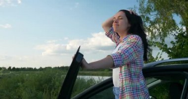 Kadın Sürücü Dinlenme Aracı 'nın yanında dinleniyor. Esmer Kadın Doğa Özgürlüğünün Taze Havası 'nın tadını çıkarıyor. Rüzgâr Esintisi Dalgalanan Saç. Yaz güneşli akşam 4K