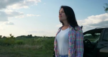 Kadın Sürücü Dinlenme Aracı 'nın yanında dinleniyor. Esmer Kadın Doğa Özgürlüğünün Taze Havası 'nın tadını çıkarıyor. Rüzgâr Esintisi Dalgalanan Saç. Yaz güneşli akşam 4K