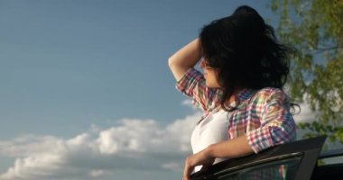 Kadın Sürücü Dinlenme Aracı 'nın yanında dinleniyor. Esmer Kadın Doğa Özgürlüğünün Taze Havası 'nın tadını çıkarıyor. Rüzgâr Esintisi Dalgalanan Saç. Yaz güneşli akşam 4K