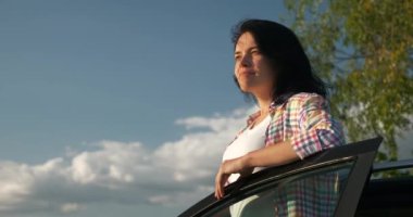 Kadın Sürücü Dinlenme Aracı 'nın yanında dinleniyor. Esmer Kadın Doğa Özgürlüğünün Taze Havası 'nın tadını çıkarıyor. Rüzgâr Esintisi Dalgalanan Saç. Yaz güneşli akşam 4K