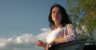 Kadın Sürücü Dinlenme Aracı 'nın yanında dinleniyor. Esmer Kadın Doğa Özgürlüğünün Taze Havası 'nın tadını çıkarıyor. Rüzgâr Esintisi Dalgalanan Saç. Yaz güneşli akşam 4K