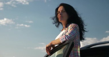 Kadın Sürücü Dinlenme Aracı 'nın yanında dinleniyor. Esmer Kadın Doğa Özgürlüğünün Taze Havası 'nın tadını çıkarıyor. Rüzgâr Esintisi Dalgalanan Saç. Yaz güneşli akşam 4K