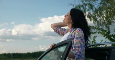 Kadın Sürücü Dinlenme Aracı 'nın yanında dinleniyor. Esmer Kadın Doğa Özgürlüğünün Taze Havası 'nın tadını çıkarıyor. Rüzgâr Esintisi Dalgalanan Saç. Yaz güneşli akşam 4K