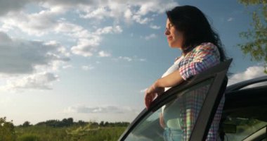 Kadın Sürücü Dinlenme Aracı 'nın yanında dinleniyor. Esmer Kadın Doğa Özgürlüğünün Taze Havası 'nın tadını çıkarıyor. Rüzgâr Esintisi Dalgalanan Saç. Yaz güneşli akşam 4K