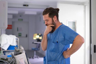 Doktor hastane ortamında duruyor, tıbbi kararları değerlendiriyor.