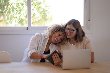 İki kadın bir dijital tablet ve dizüstü bilgisayarı paylaşıyor, gülümsüyor, aşkı ve birlikteliği temsil ediyor.
