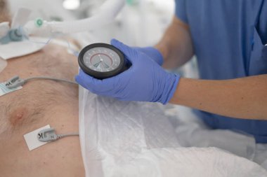 Yoğun bakımda olan solunum cihazındaki bir hastanın basınç göstergesini kontrol eden profesyonel eller.