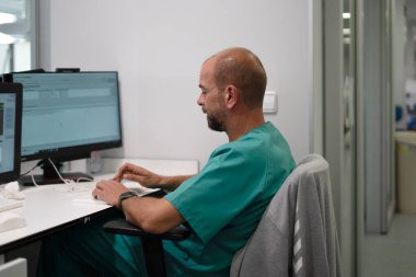 Sağlık uzmanı bilgisayar üzerinde çalışıyor, klinikte tıbbi verileri analiz ediyor.