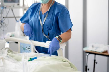 Yoğun bakım ünitesindeki bir hastaya ameliyat önlüğü ve eldiven giyen bir sağlık uzmanı bakıyor.