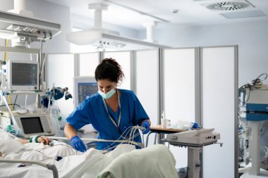 Yoğun bakımda yatalak bir hastaya bağlı tıbbi ekipmanları kontrol eden sağlık uzmanı.