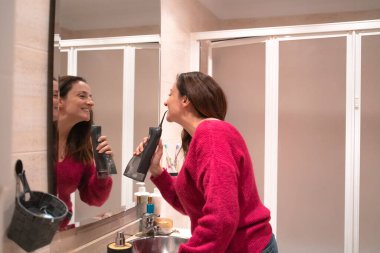 Banyoda duran bir kadın aynaya bakıyor. Ağız bakımı için diş ipi kullanıyor.