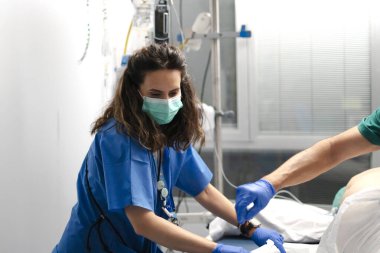 Hastane odasındaki bir hastaya ameliyat önlüğü ve maske takan hemşire...