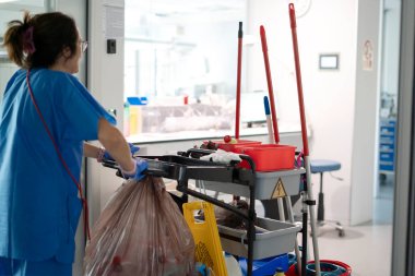 Mavi üniformalı ve eldivenli temizlikçi.